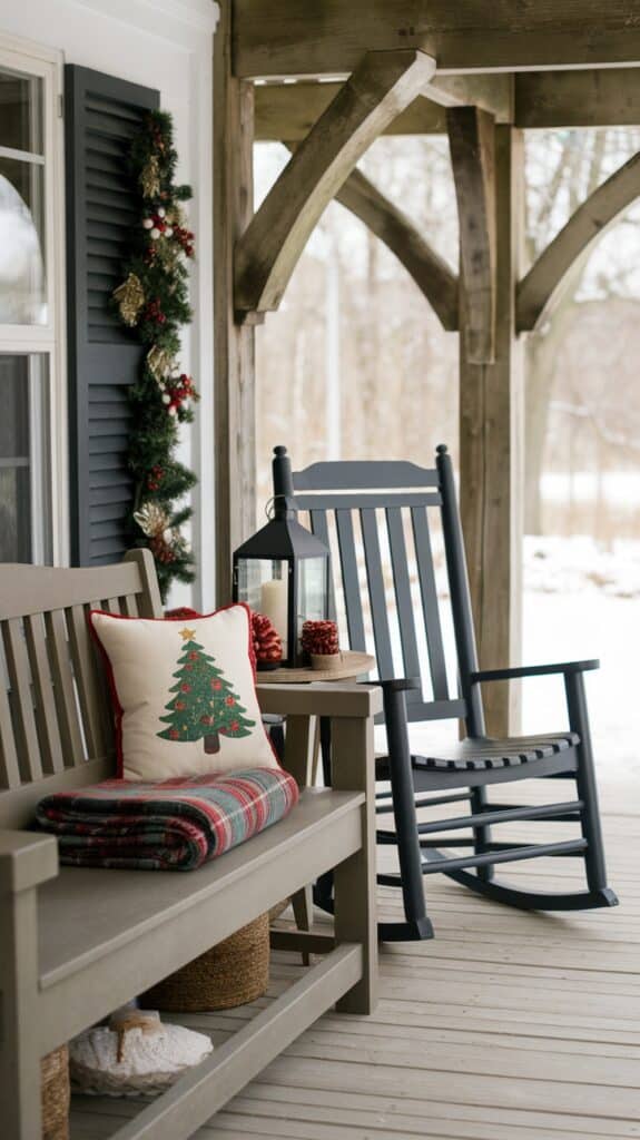A cozy porch decorated for the holiday season with a wooden bench and rocking chair. The bench features a plaid blanket and a cushion with a Christmas tree design. A lantern with candles sits on a small table next to the rocking chair. Garland and festive decorations adorn the wall.