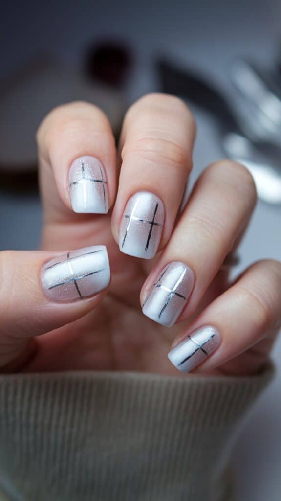 Close-up of a hand with a manicure featuring a white shimmering nail polish and a black grid design on each nail.