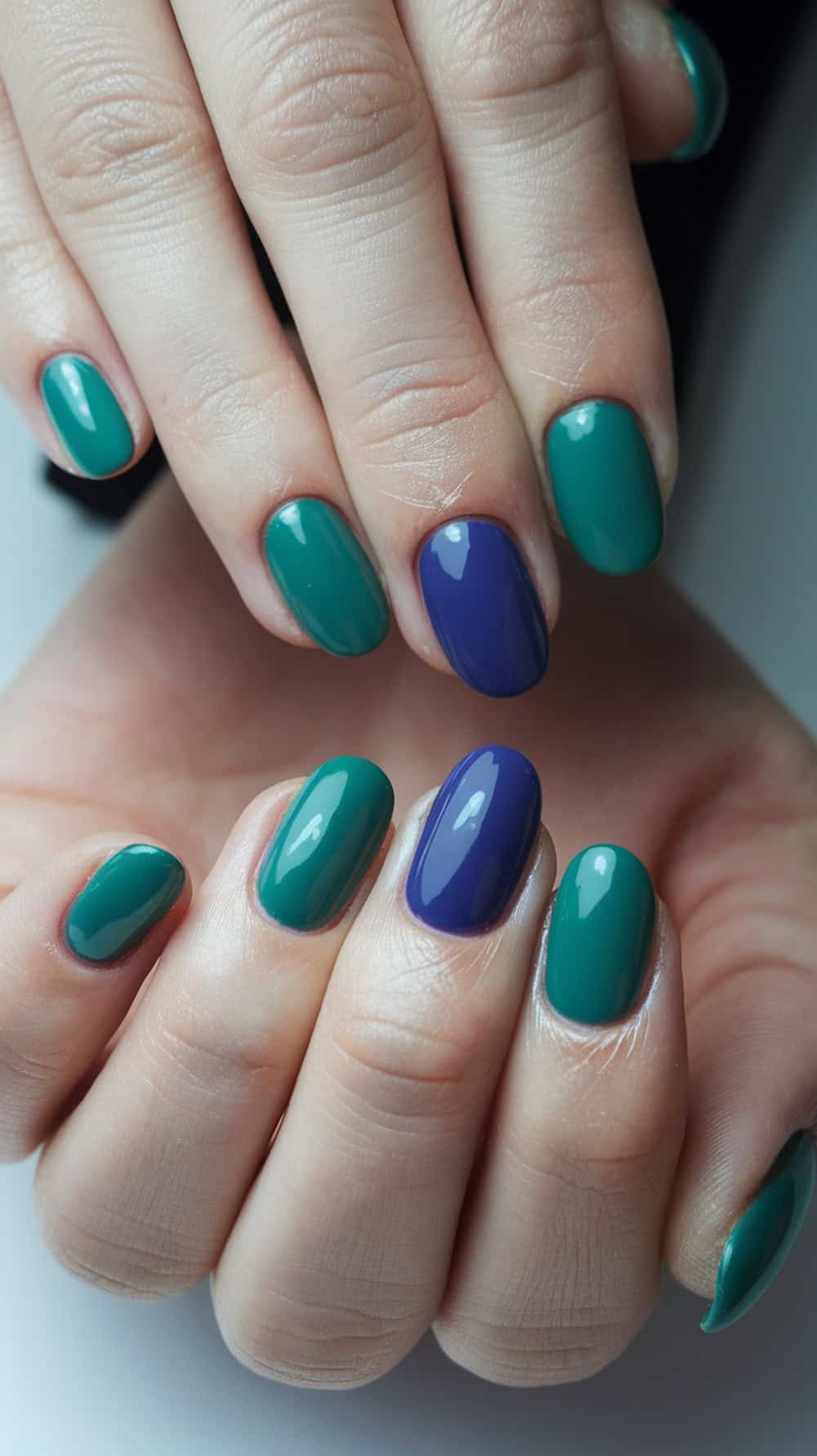 Hands with nails painted in alternating teal and purple colors.