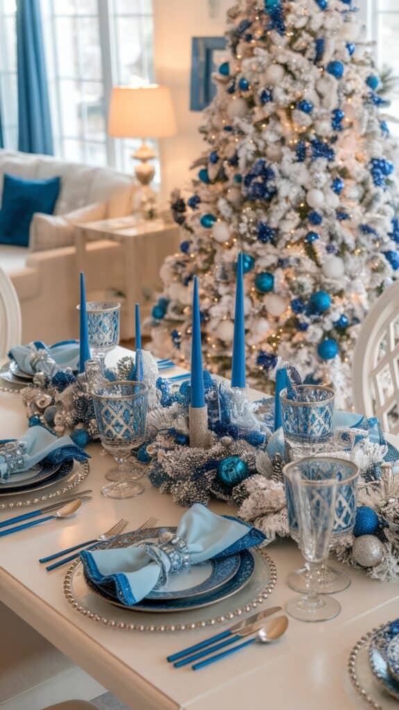 A elegantly set dining table decorated with blue and silver holiday-themed accessories, including deep blue candles, ornate glassware, and blue napkins, against the backdrop of a Christmas tree adorned with blue and white ornaments.