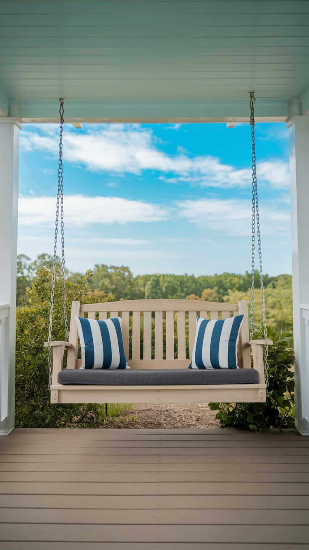 A wooden porch swing with blue and white striped cushions overlooks a lush green landscape and sky.